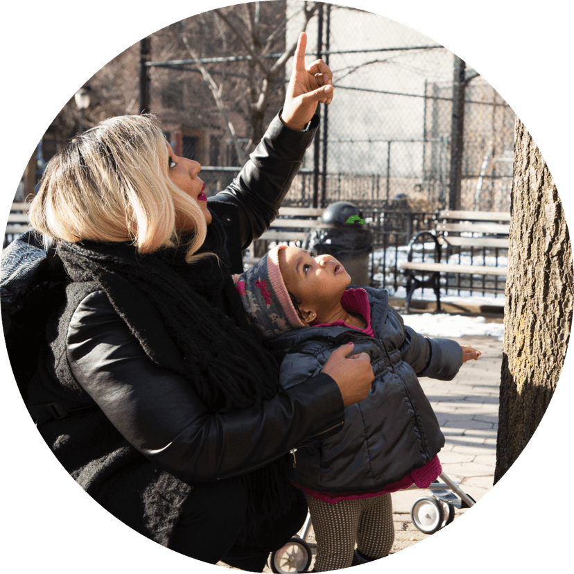 A mother points to something in a tree above and her child looks up to see what it is.